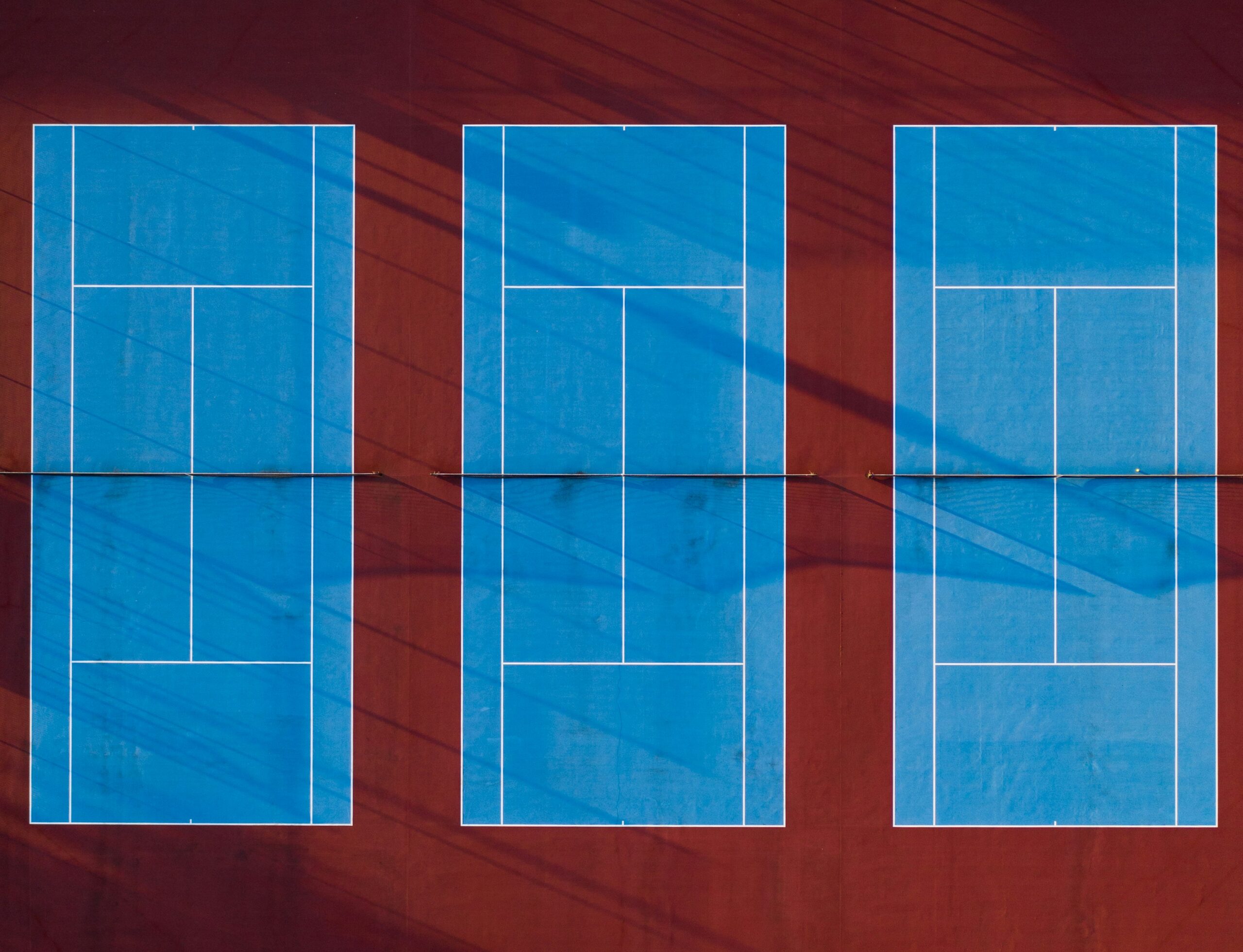 Aerial view of three school tennis courts showing court markings, run-off space and orientation