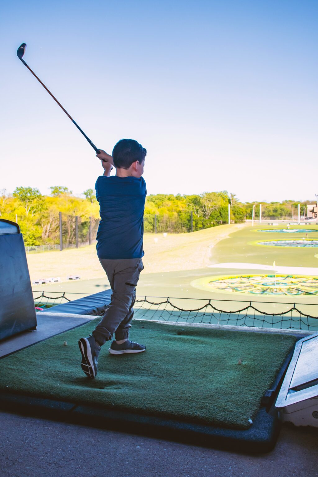Young boy swinging a golf club on a driving range